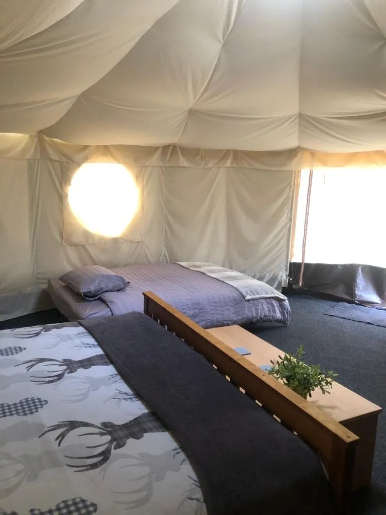 Interior of a glamping tent with two beds, a round window, and a small wooden table.