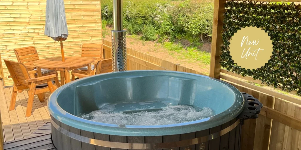 A bubbling hot tub on a wooden deck with a table, chairs, and a parasol.